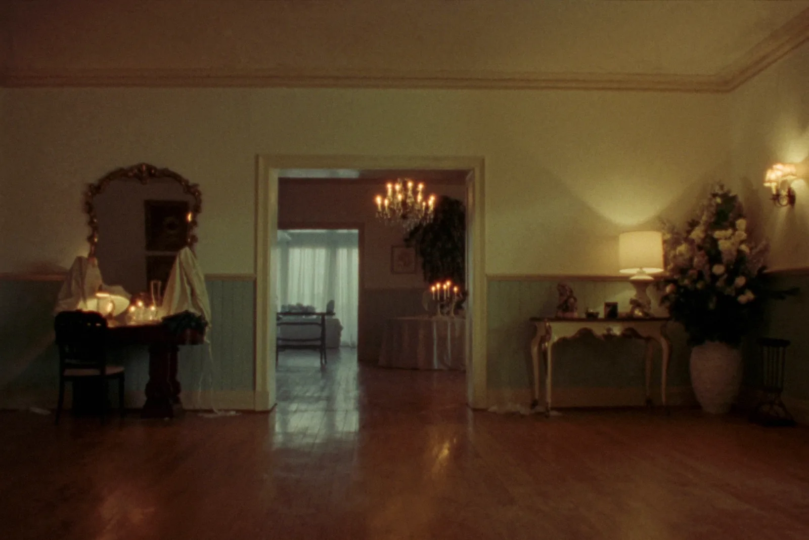 An elegant venue foyer at dusk, an open doorway glowing through to a candlelit reception room beyond