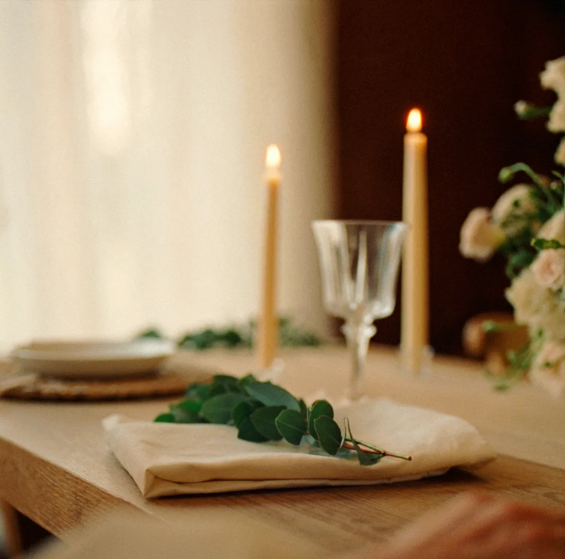 A wedding place setting in warm candlelight — linen, eucalyptus, taper candles and crystal glass